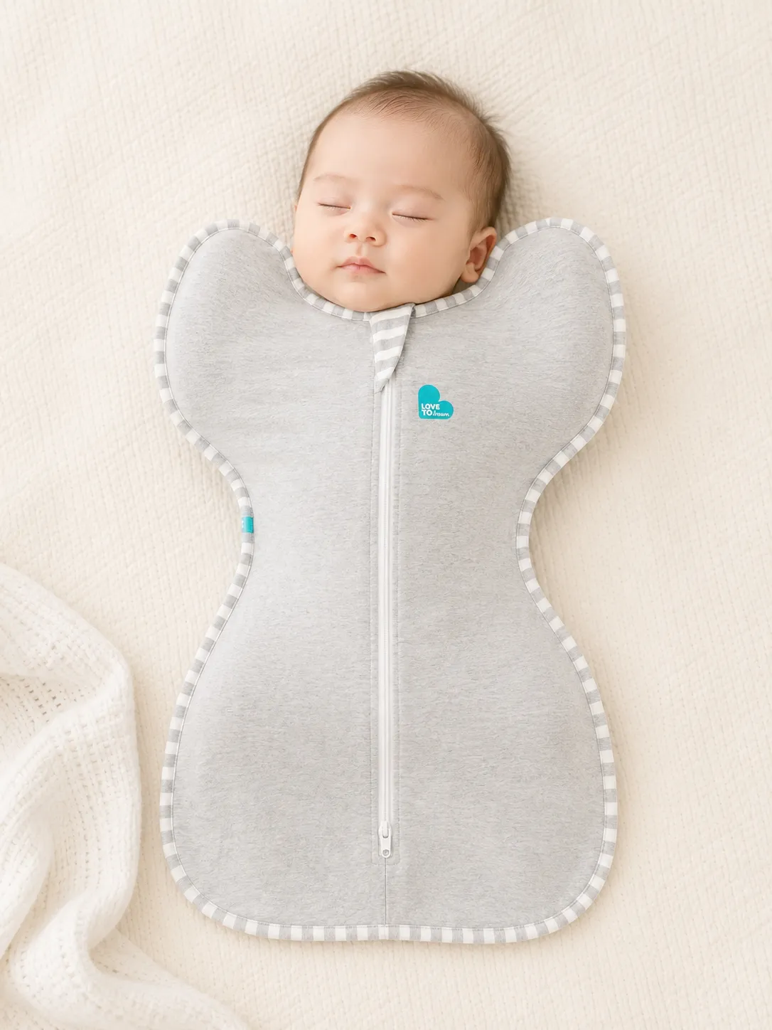 Newborn baby wearing Love to Dream SwaddleUp swaddle. Arms are in the natural W-position raised alongside the face, with wing pockets keeping hands near mouth for self-soothing.