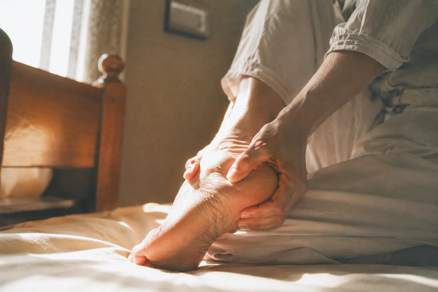 아침에 일어나 첫발을 디디며 발뒤꿈치 통증으로 발을 감싸 쥐는 사람의 모습, 족저근막염 증상을 표현한 이미지