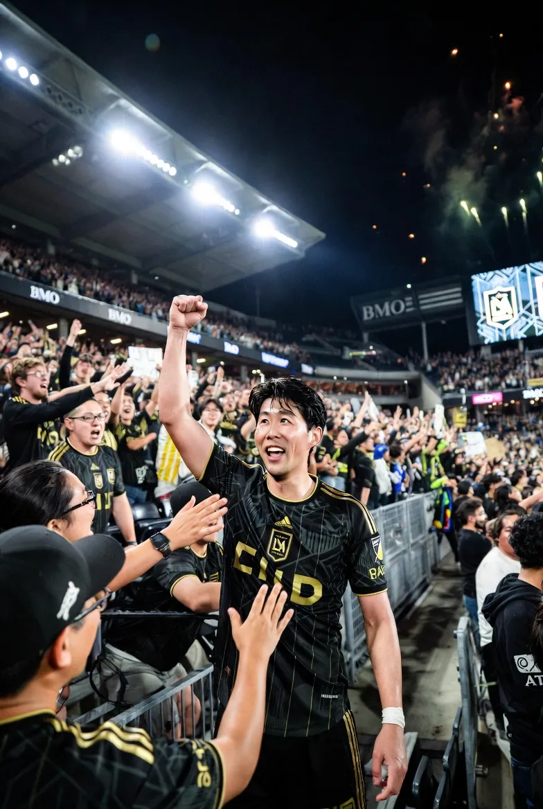 LAFC 스타디움에서 손흥민이 검은색과 금색 유니폼을 입고 팬들과 함께 환호하는 모습, 배경에 BMO 스타디움의 불꽃놀이와 군중의 열기가 느껴지는 역동적인 경기장 풍경